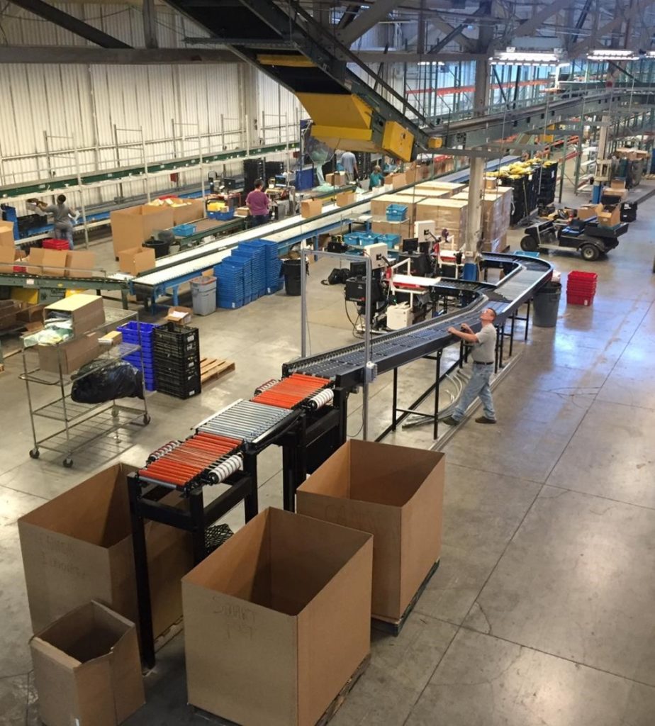 a wide perspective image of an eSort system in action at a warehouse with several workers monitoring and working with the system.